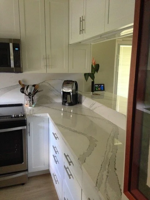 Kitchen with white cabinets, a black coffee maker, a microwave, and a vase with a flower on the countertop.