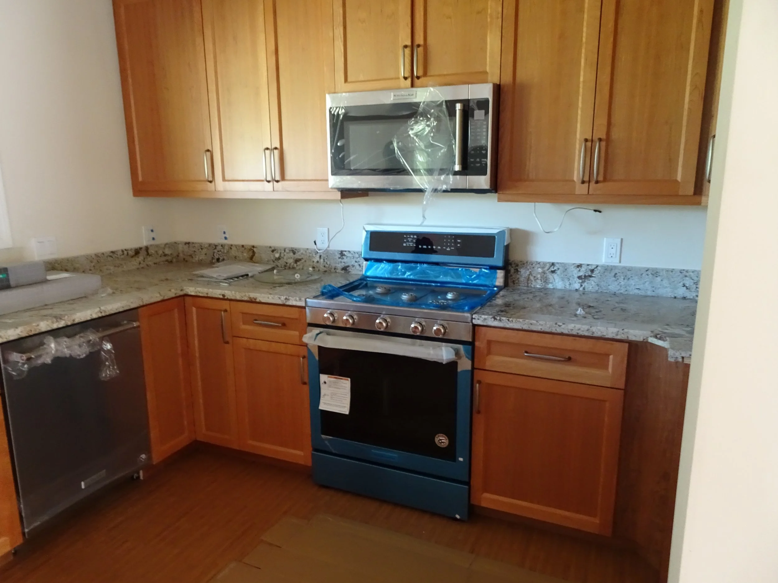 Kitchen with wooden cabinets, granite countertops, stainless steel microwave and stove, and a dishwasher, appears to be newly installed.