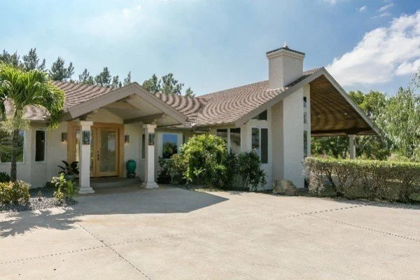 Front view of a modern house with a driveway, white exterior walls, a covered entrance, and surrounded by greenery.