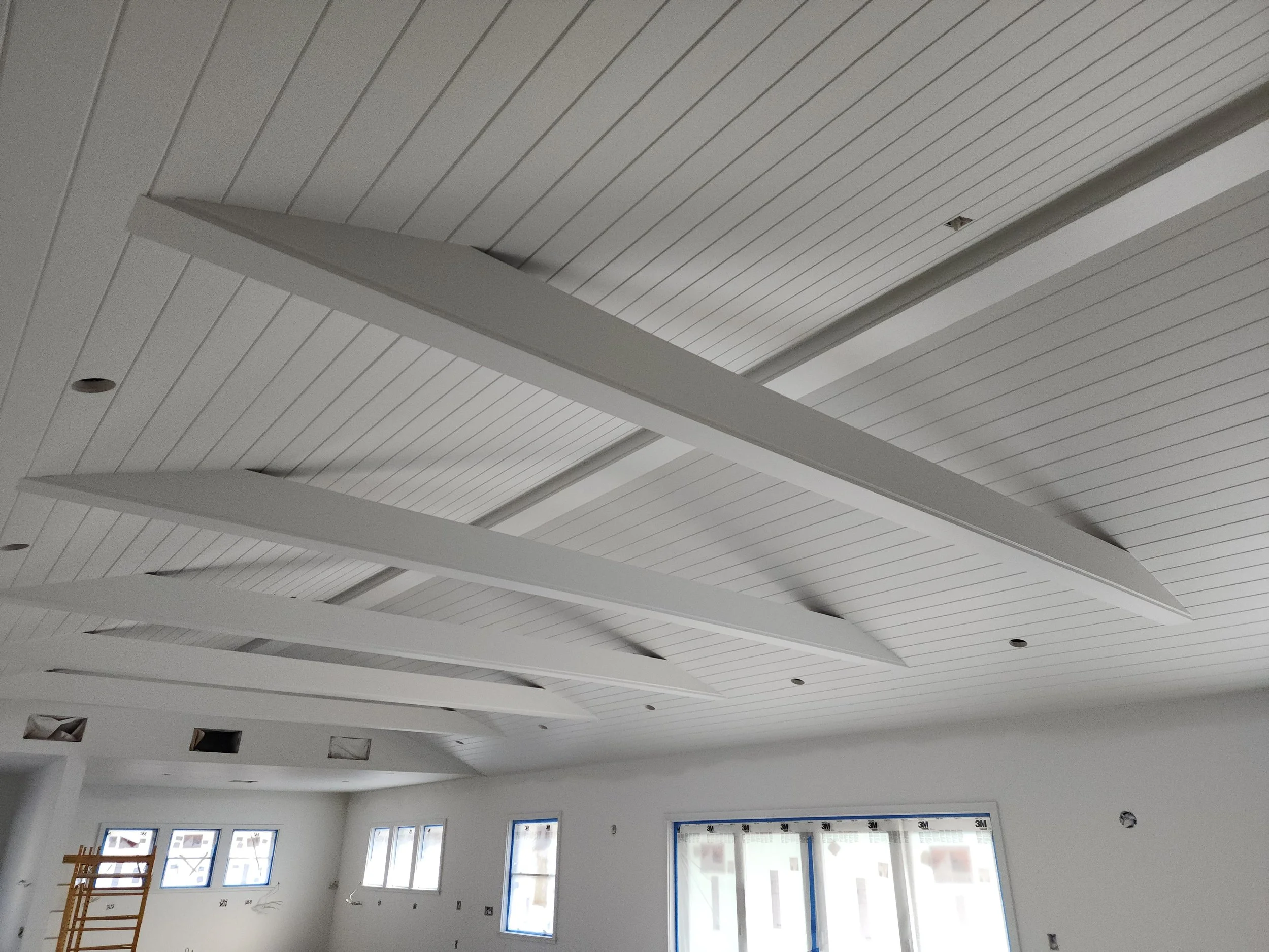 Ceiling with white paneling and modern suspended light fixtures in a room under construction.