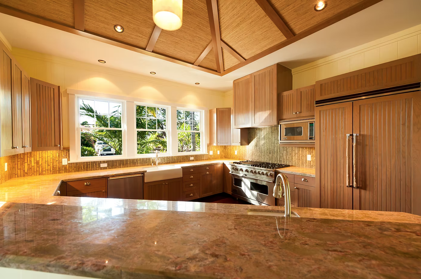 Bright kitchen with wooden cabinets, granite countertops, and a large window showing outdoor greenery. Contains stainless steel appliances including a microwave, oven, and refrigerator.