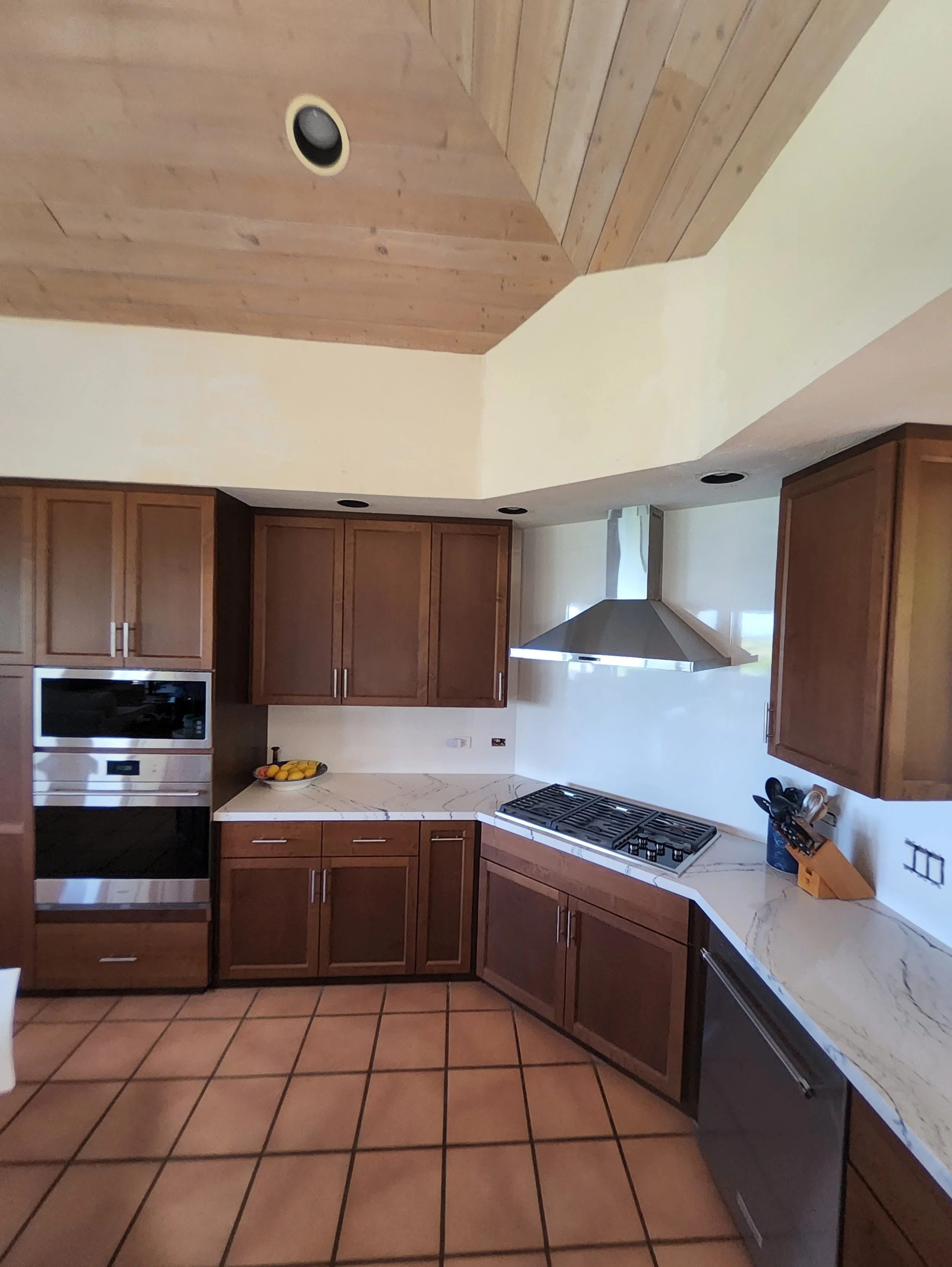 Kitchen with brown wooden cabinets, a built-in oven, a gas stovetop, a silver range hood, and tiled floor.