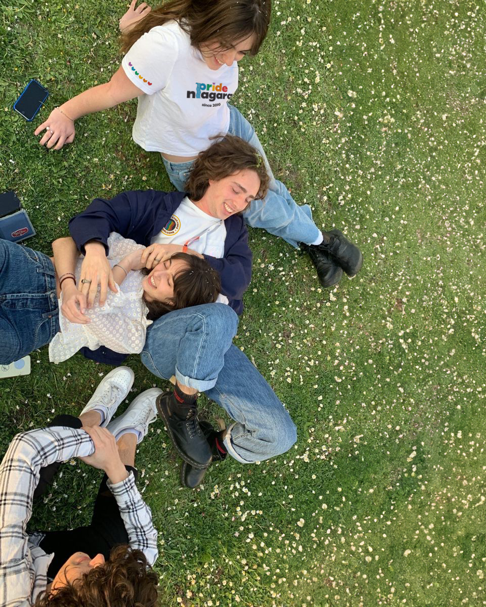 Caucasian friends laying in the grass wearing Pride Niagara t-shirts, designed by Steph Parker Designs