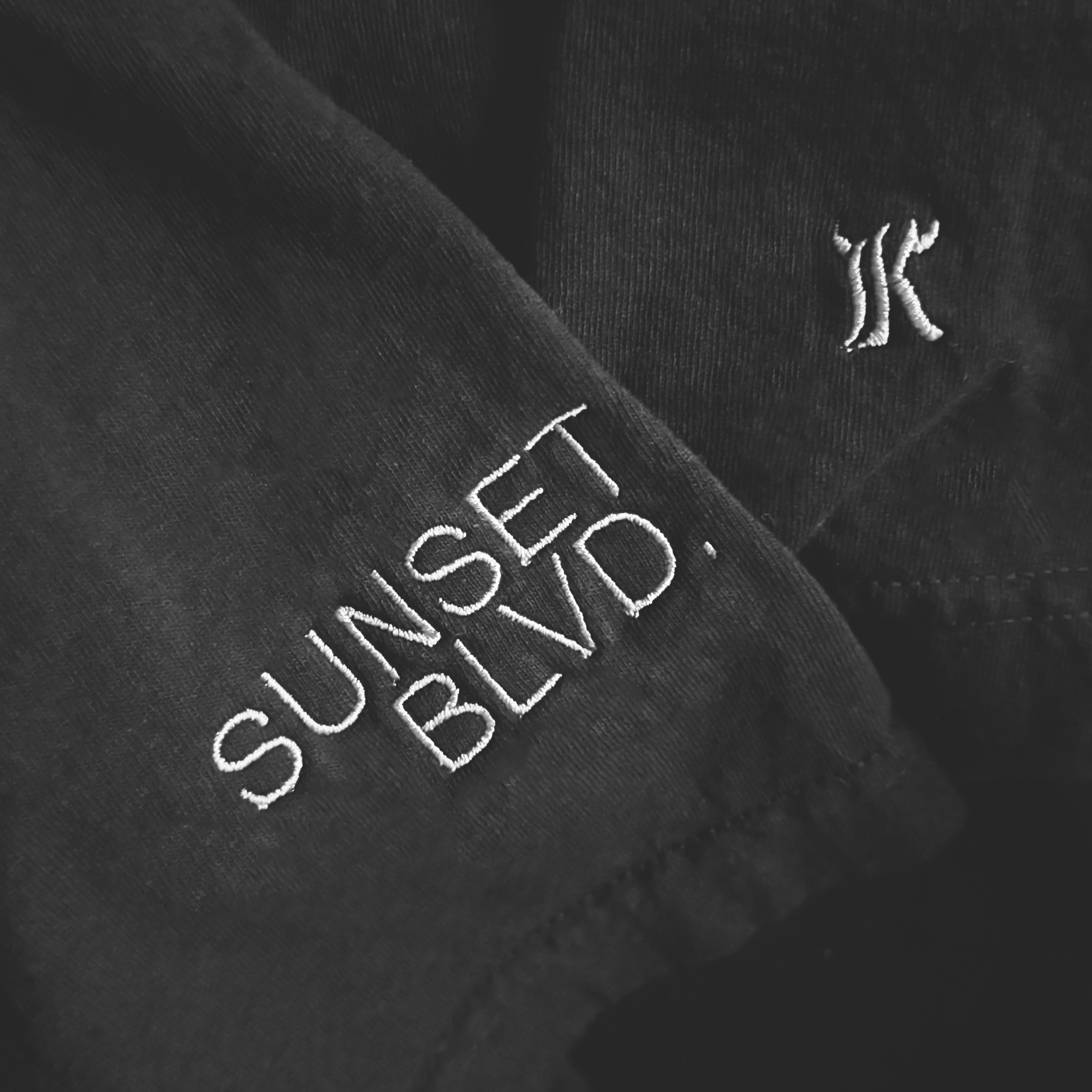 Close-up of black fabric with white embroidered text reading 'SUNDSET BLVD.' and a small embroidered 'K' Ker Co. logo.