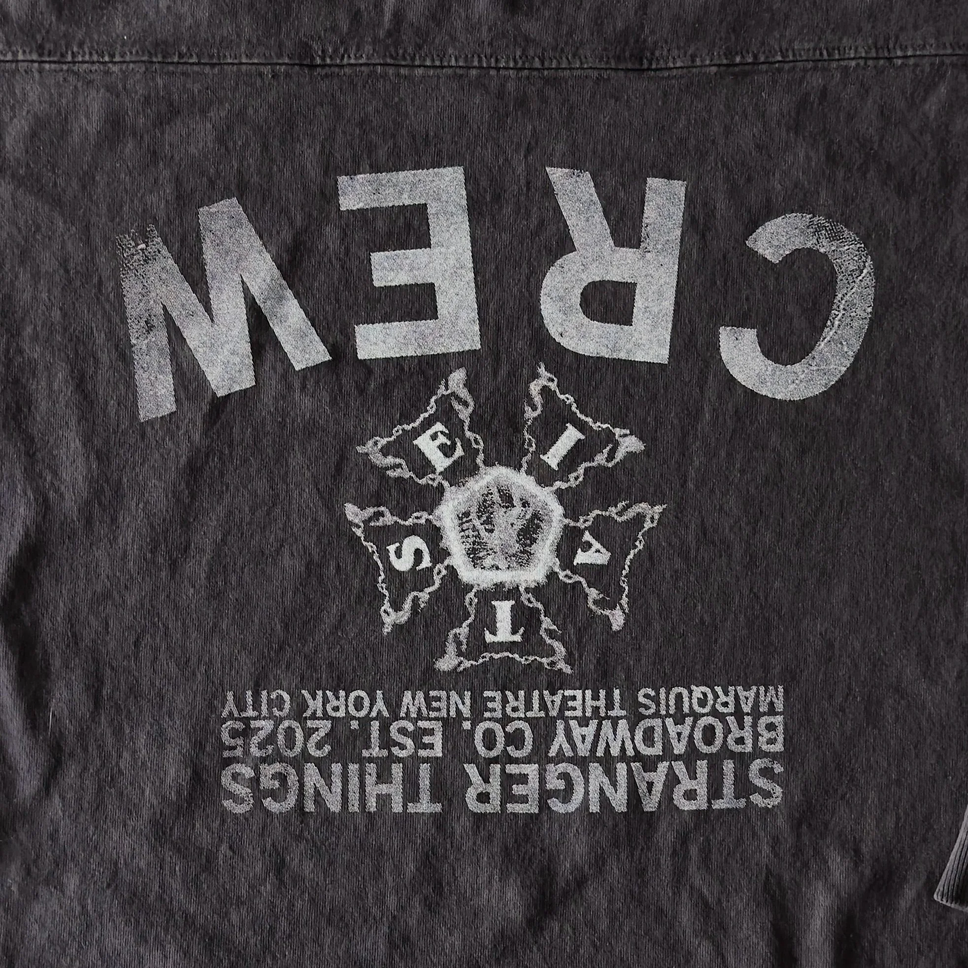Close-up of a dark gray T-shirt with white printed text and graphics. The text includes 'SILVER THINGS' and 'BEDFORD, CO. - EST. 2025'. There is a central graphic of a skull surrounded by a star.