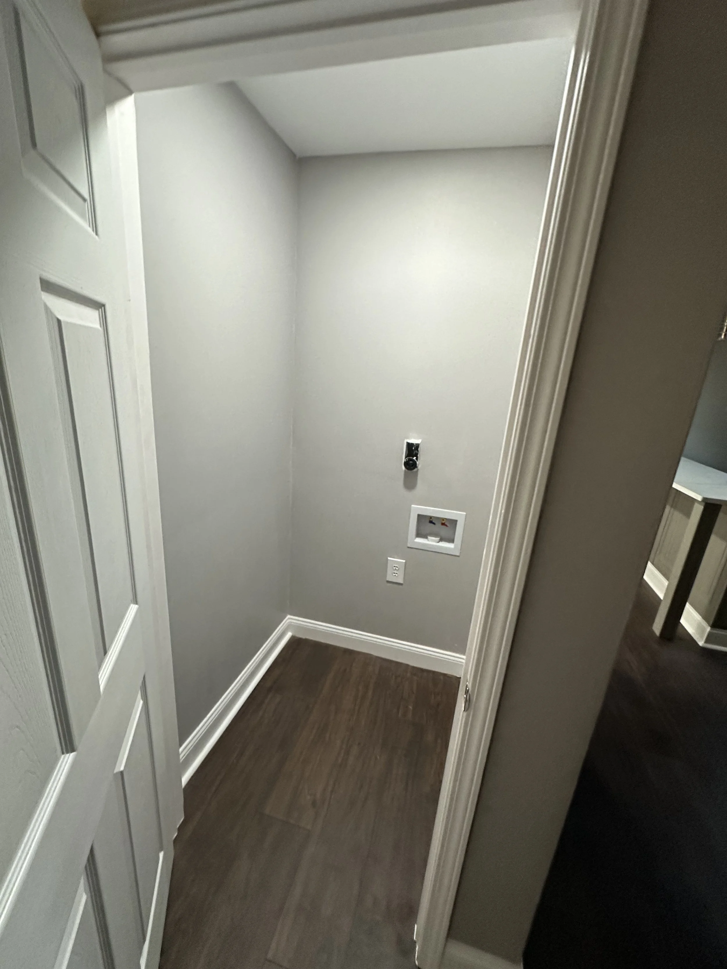 Empty laundry nook with gray walls, dark wood flooring, and connections for a washer and dryer.