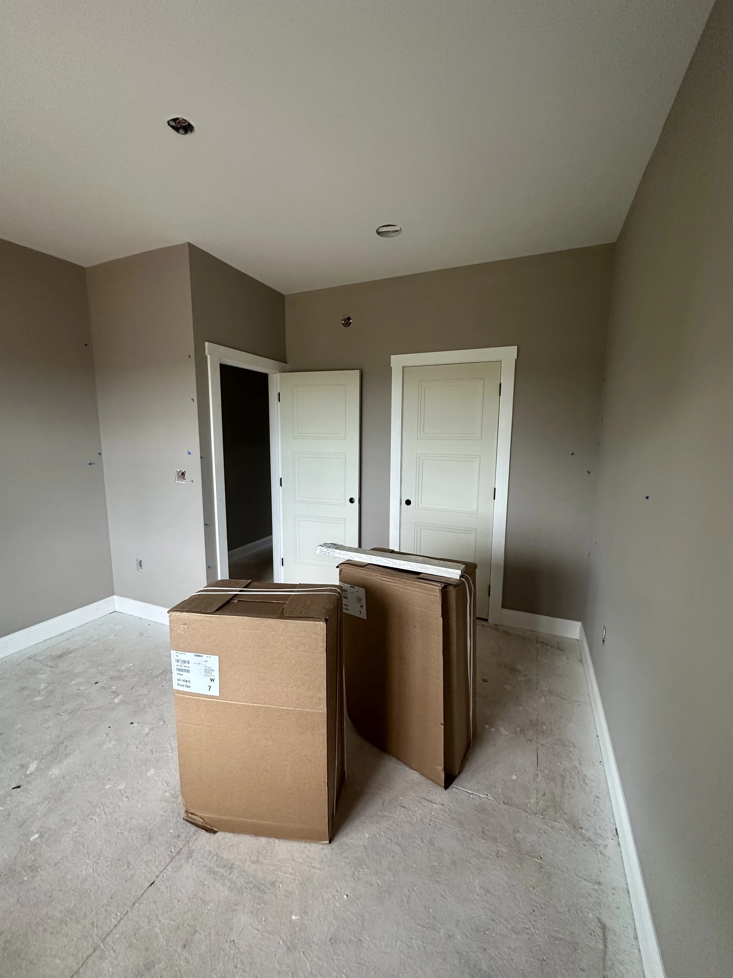 An unfinished room with two cardboard boxes on the floor and two closed closet doors.