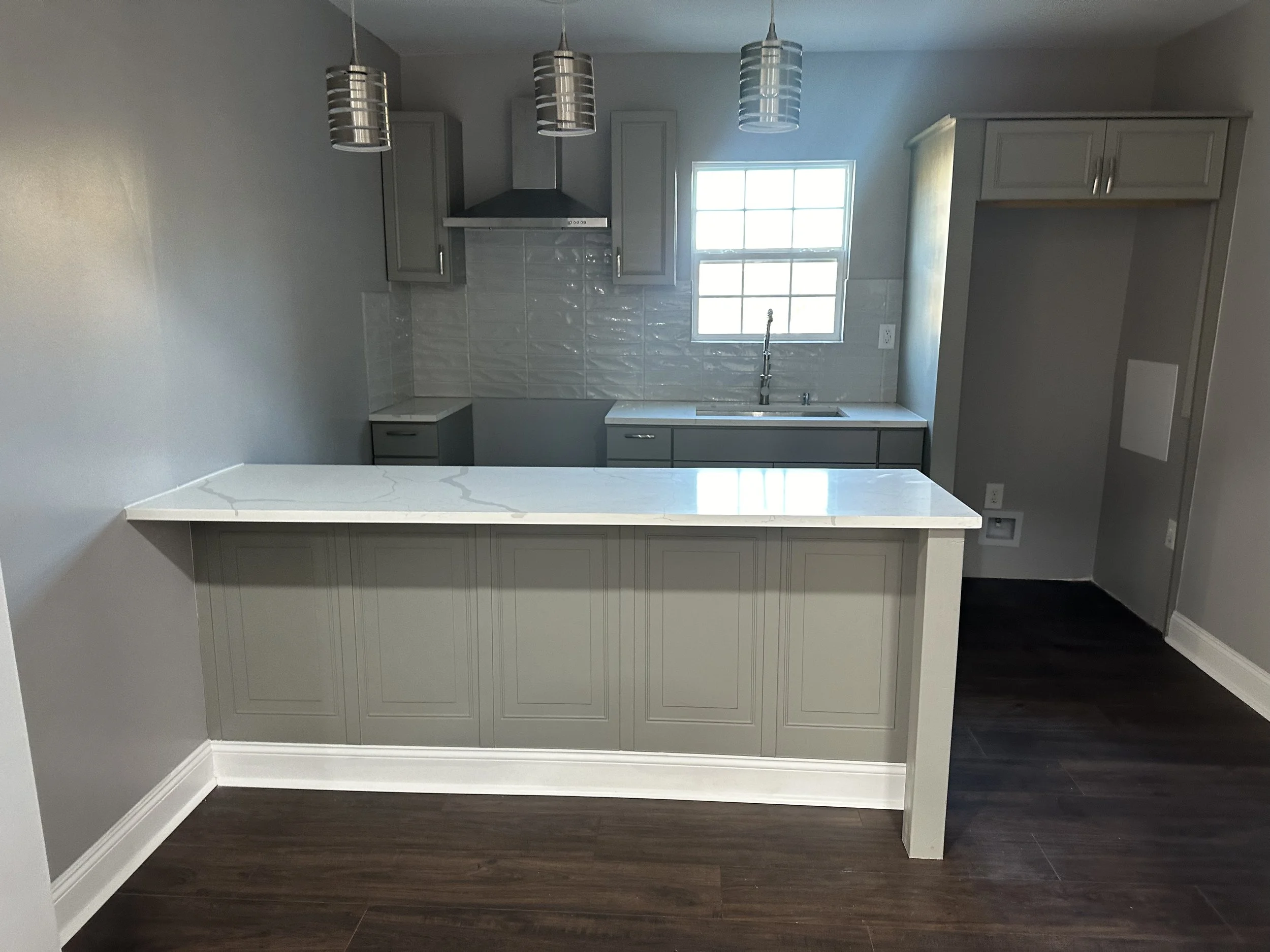 Modern kitchen with light grey cabinets, a white marble countertop island, a window above the sink, and three pendant lights hanging from the ceiling.