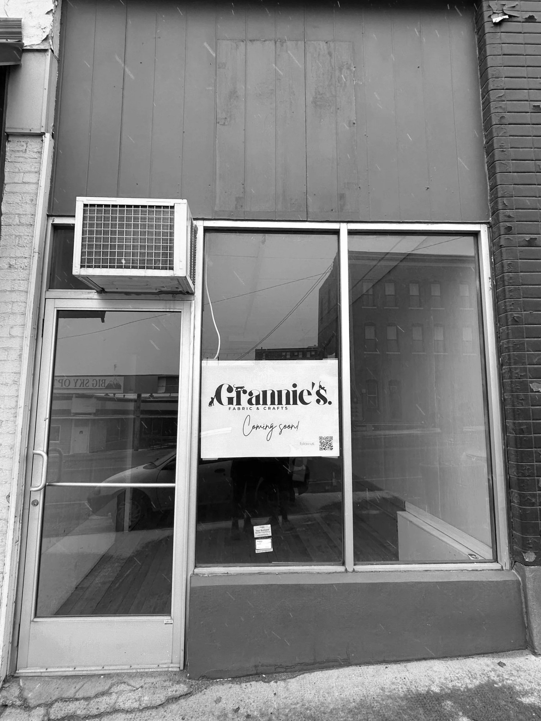Empty storefront with a sign that says 'Grannie's Fabric & Crafts' coming soon, with a glass door and window.