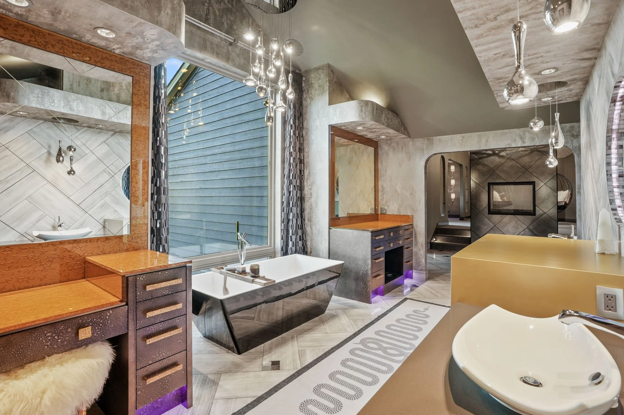 Modern bathroom with a freestanding bathtub beneath a large window, metallic hanging lights, a yellow countertop with a white sink, and various textured walls and decor