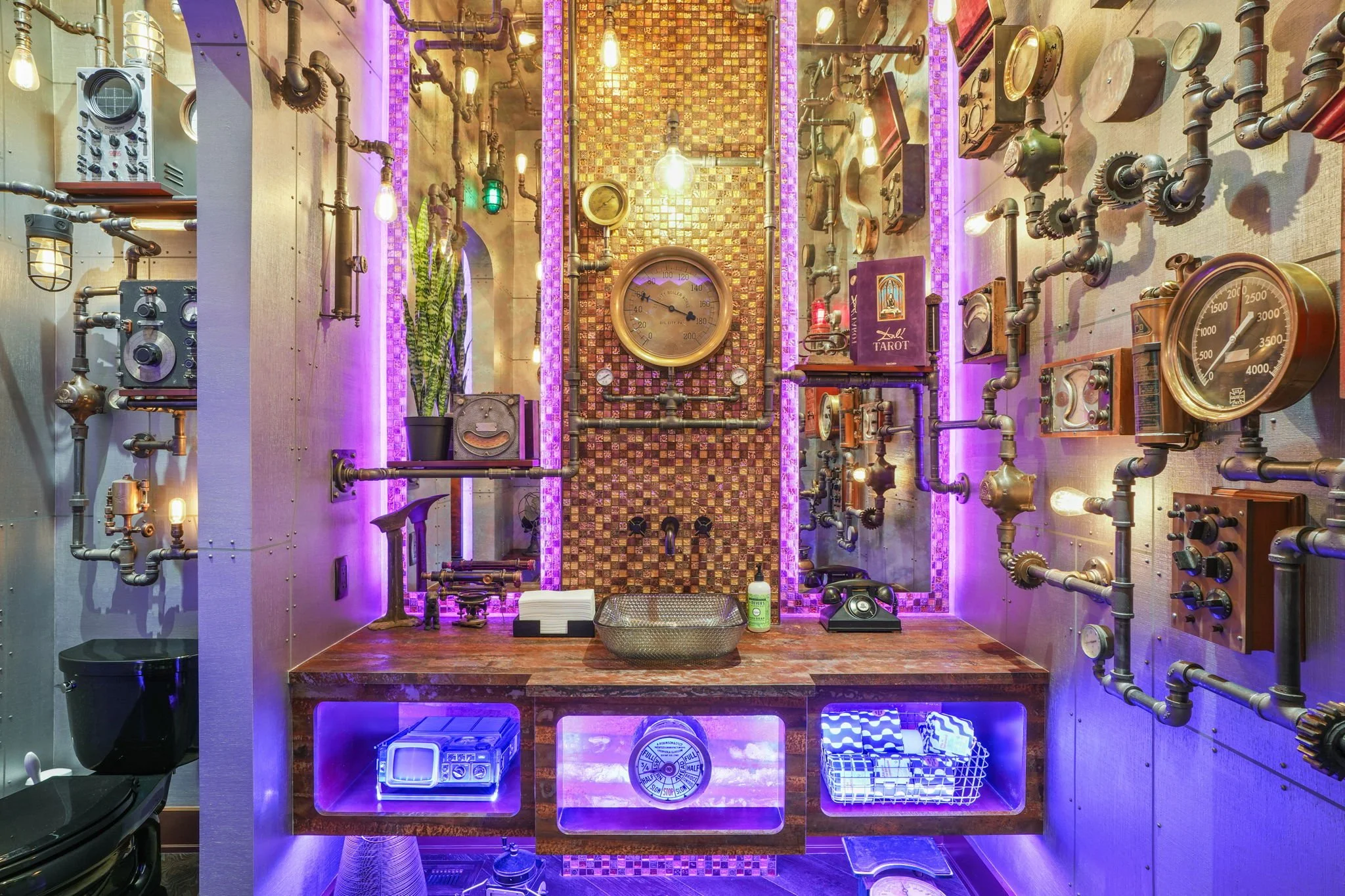 A room with a steampunk style featuring an array of exposed pipes, gauges, and vintage mechanical devices. The wall behind has colorful tile and purple neon lighting. A countertop with a metal basin, a potted plant, and various items, including an ol