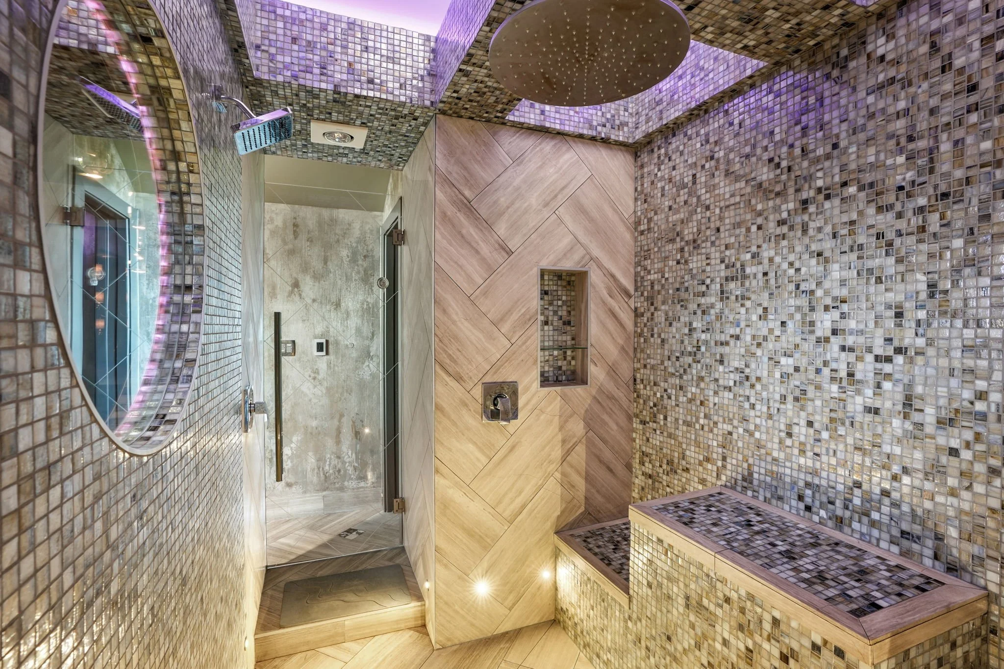 Modern bathroom with mosaic tile walls and ceiling, wood-paneled shower area, glass door, and a round mirror.