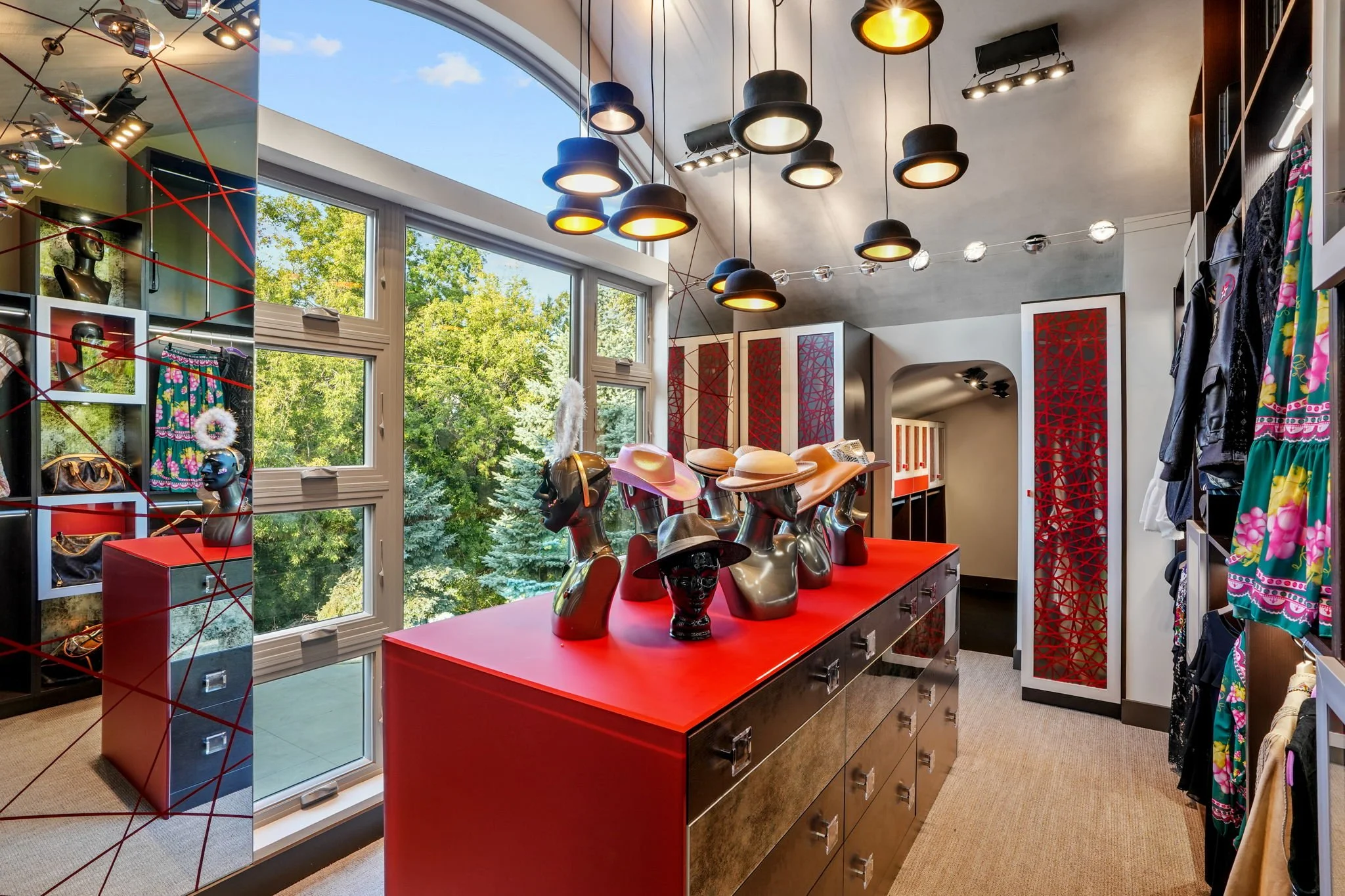 A boutique displays mannequin heads with hats on a red counter, surrounded by clothing and accessories, with large windows showing green trees outside.
