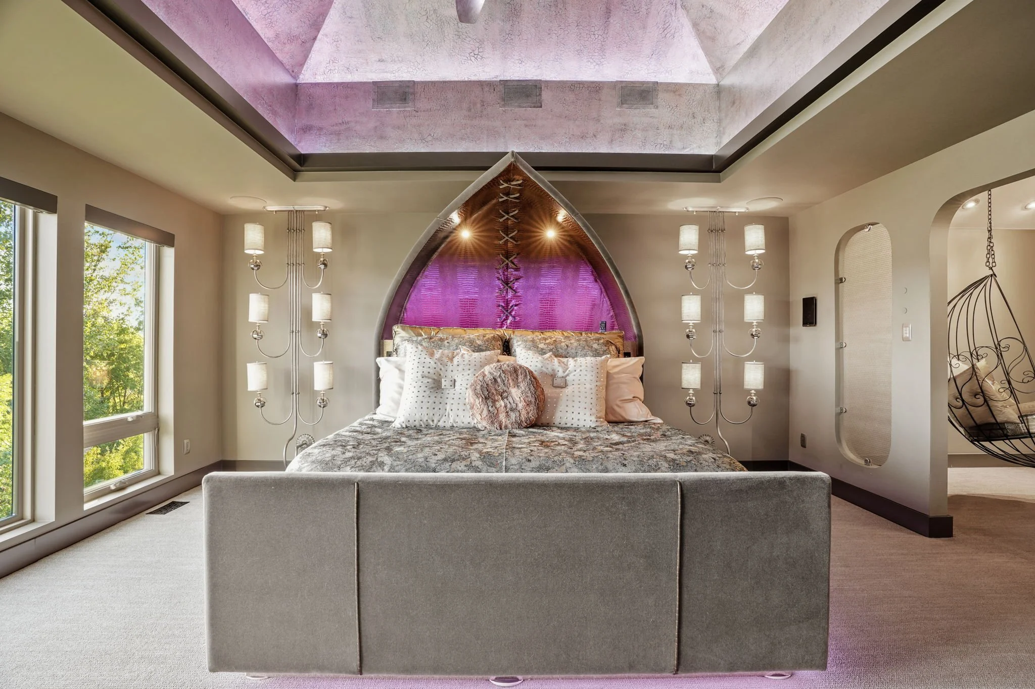 A modern bedroom with a large bed, purple and pink accents, and contemporary lighting fixtures.