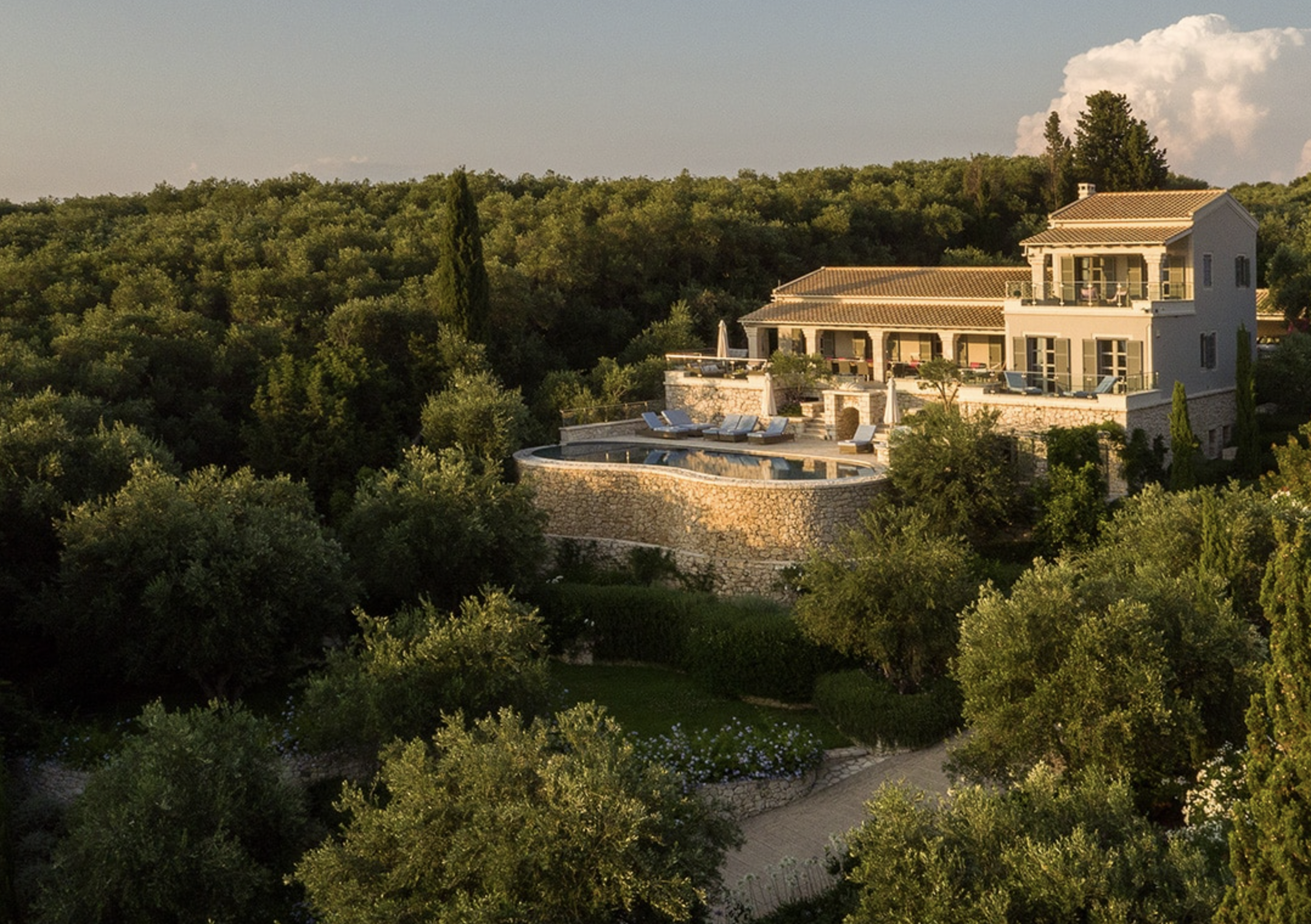 Luxury house on a hillside with a swimming pool and surrounding greenery during sunset.