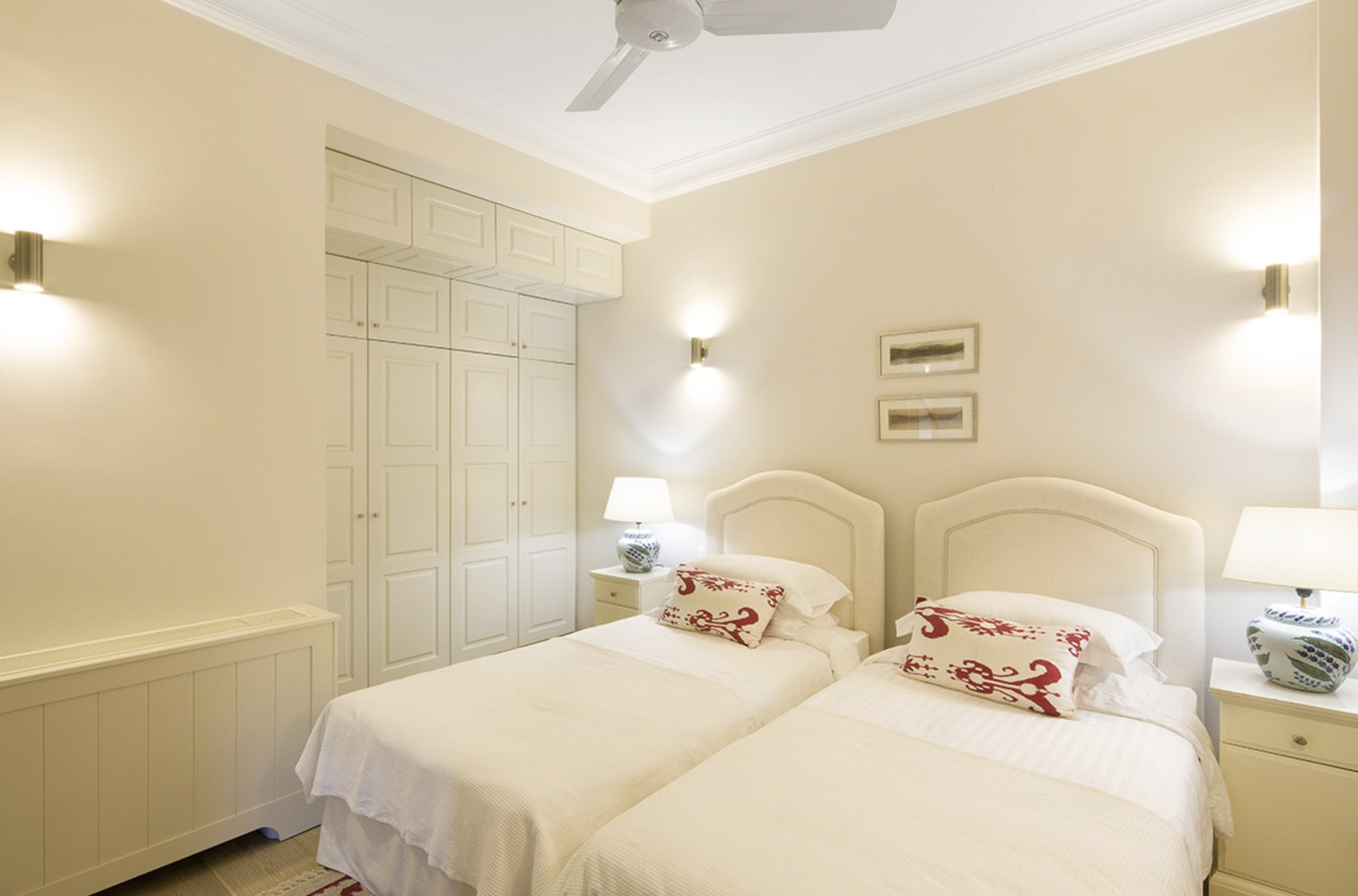 Hotel bedroom with two twin beds, white headboards, white linens, patterned pillows, bedside lamps, beige walls, and built-in closet.