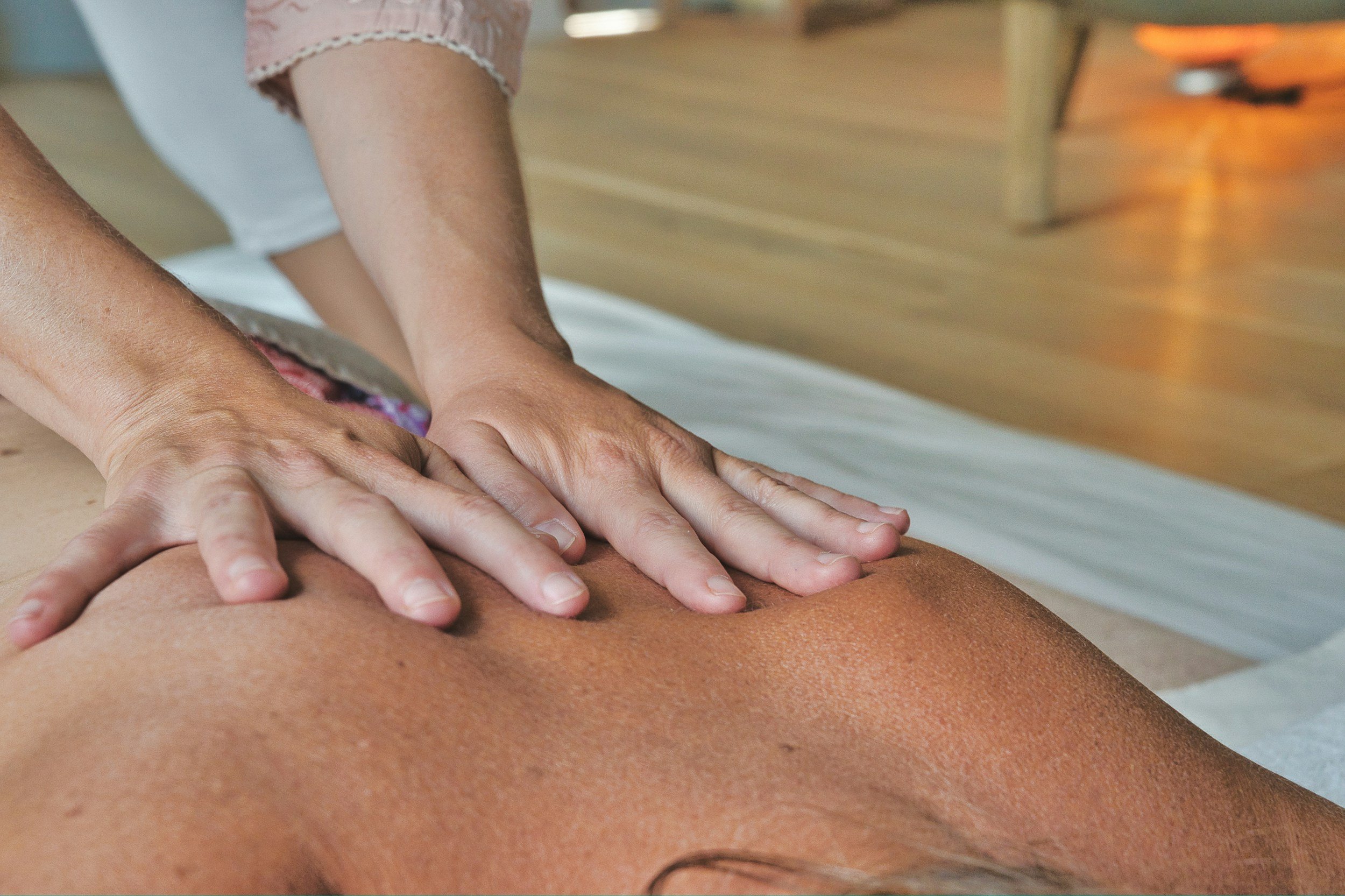 Person receiving a massage, lying face down on a massage table, with hands pressing on their back.