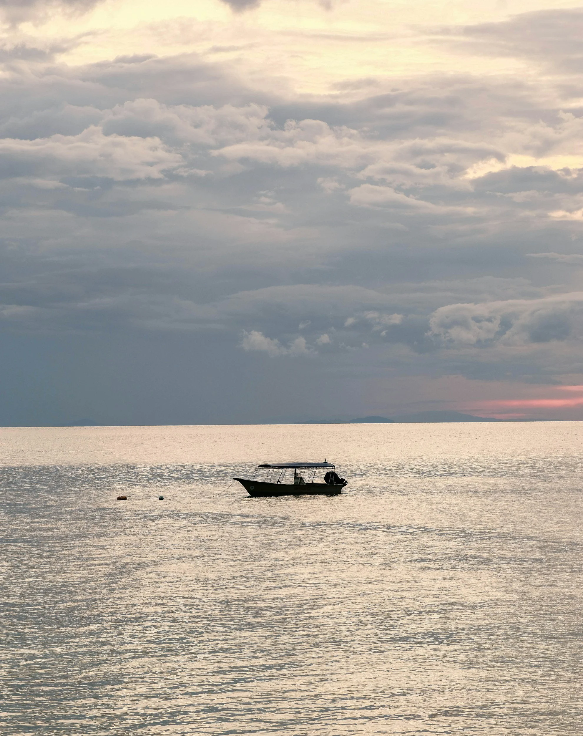 A boat floating on calm water during sunset with cloudy sky overhead.