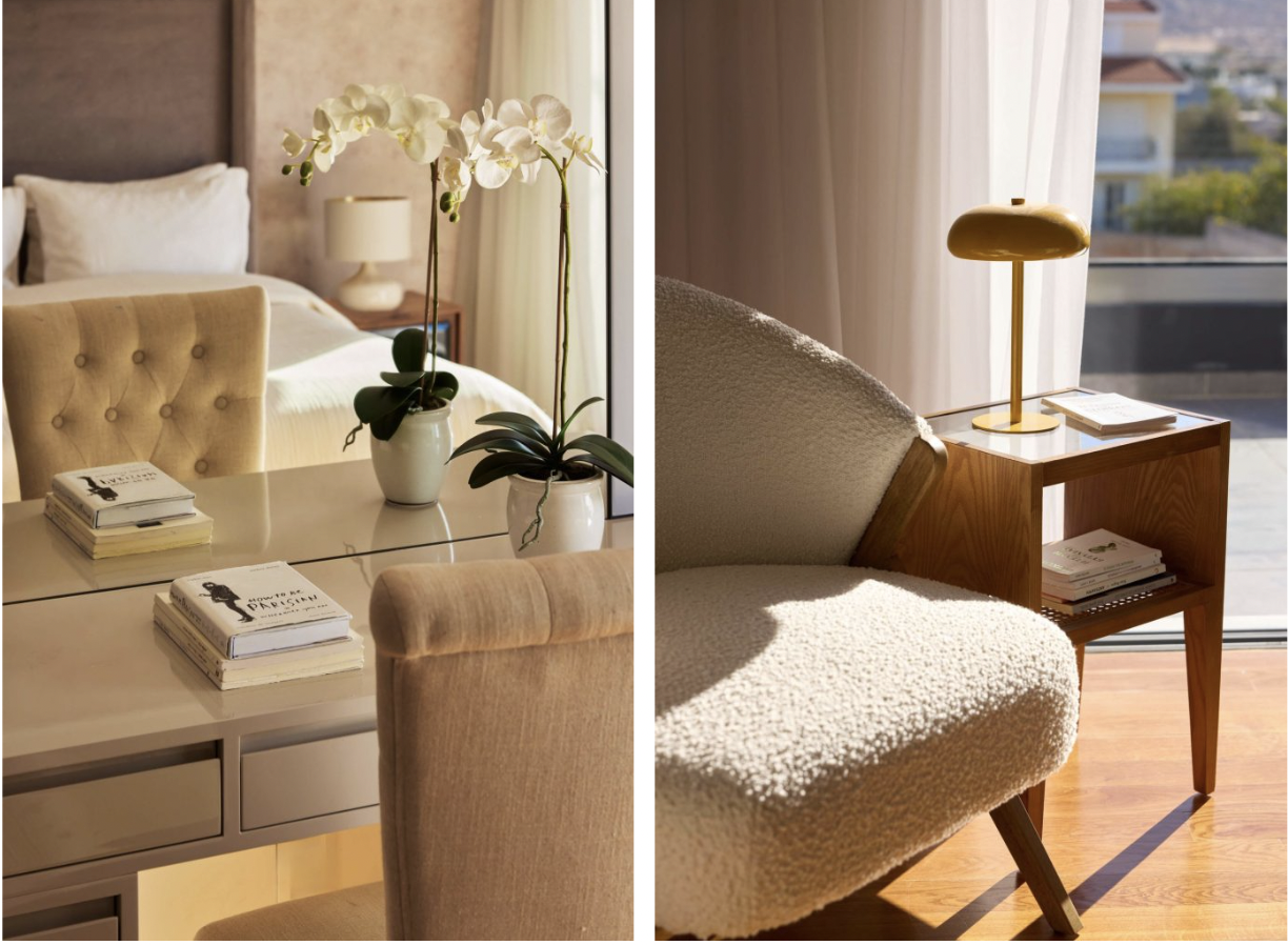 Interior of a bedroom with white bedding, a nightstand with a lamp, and a large window with curtains on the left. A table with a potted orchid and a book is in the foreground. On the right, a cozy armchair with a side table with a lamp and books, near a sliding glass door letting in sunlight.