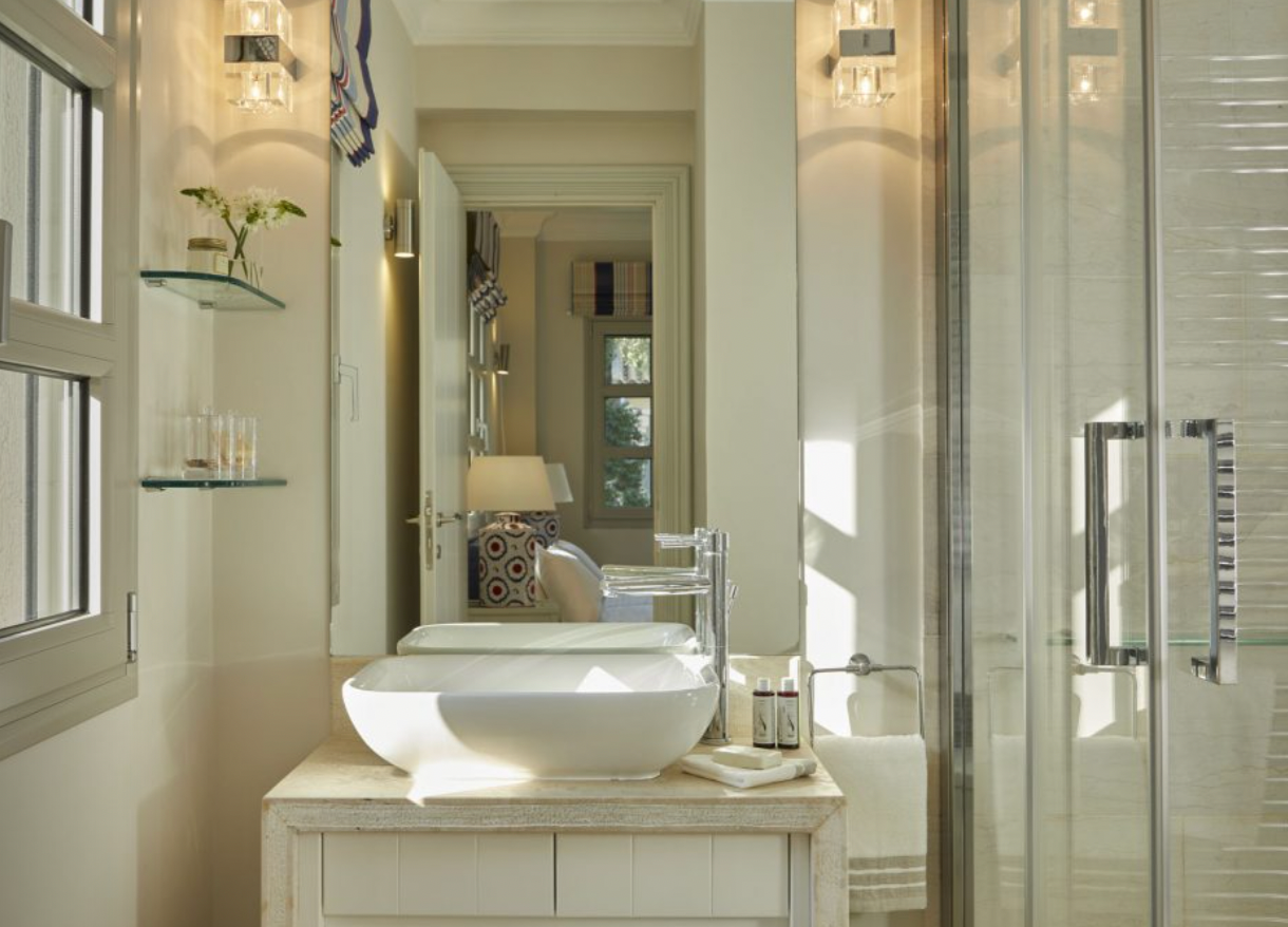 A bright, airy bathroom with a modern sink, glass shower enclosure, window, and decorative lighting.