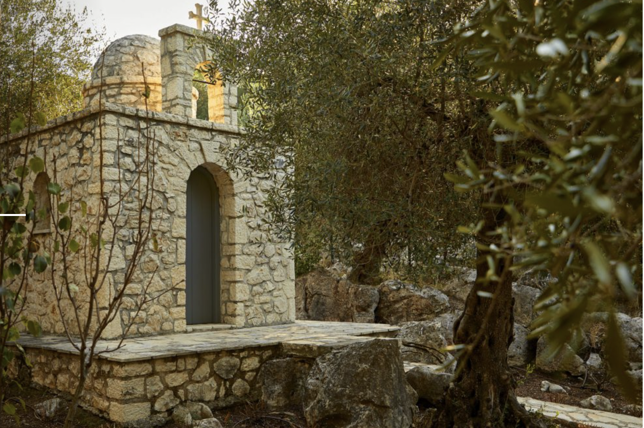 Small stone chapel with a cross on top, in a natural setting with trees and rocks around.
