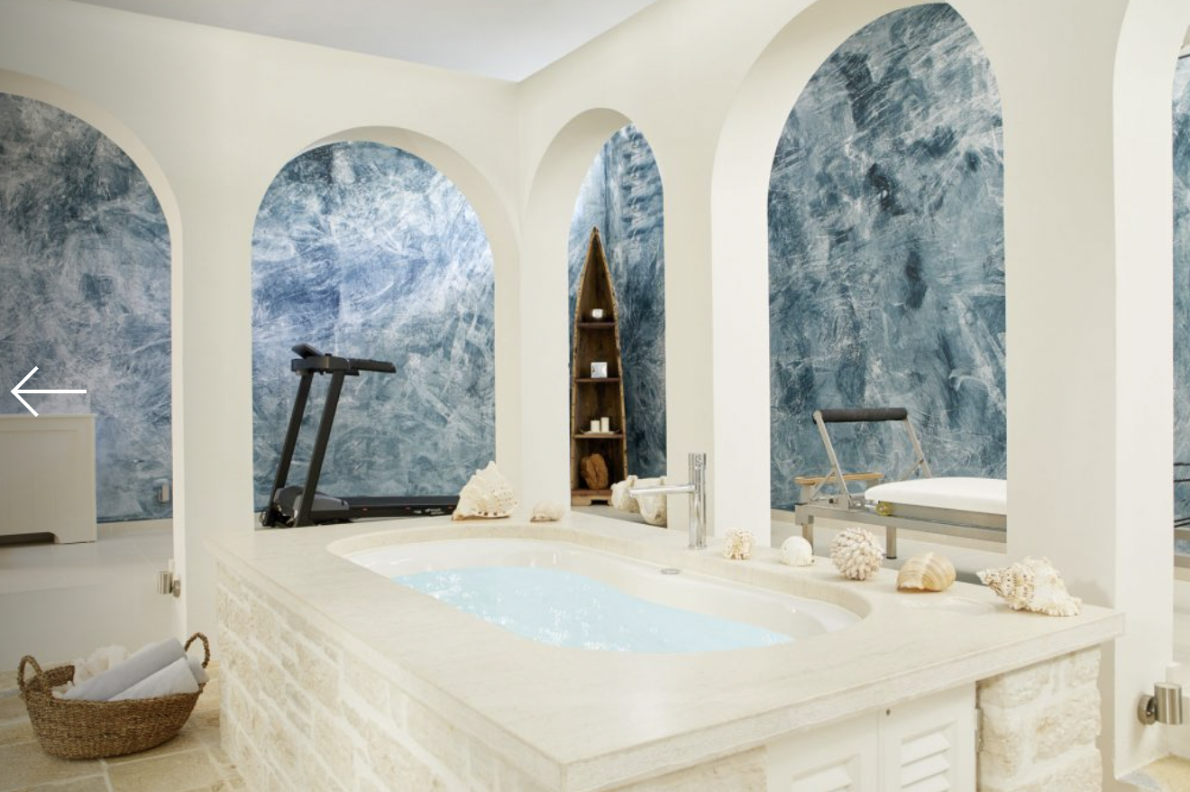 Luxurious bathroom with a built-in hot tub, decorated with seashells and marine ornaments, featuring arched blue marble walls and a treadmill in the background.