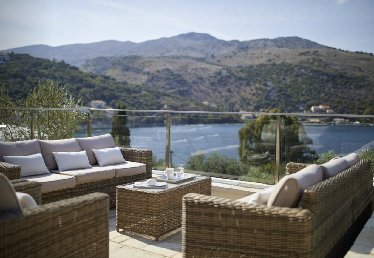 Outdoor patio with wicker furniture, glass of water, and scenic view of a lake and mountains in the background.