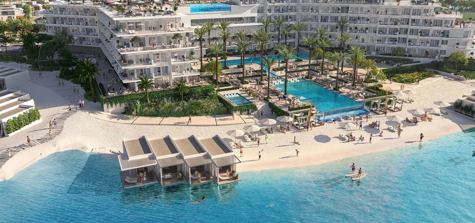 Aerial view of a luxurious beachside resort with multiple pools and sunbathing areas, palm trees, and a modern white building with balconies.
