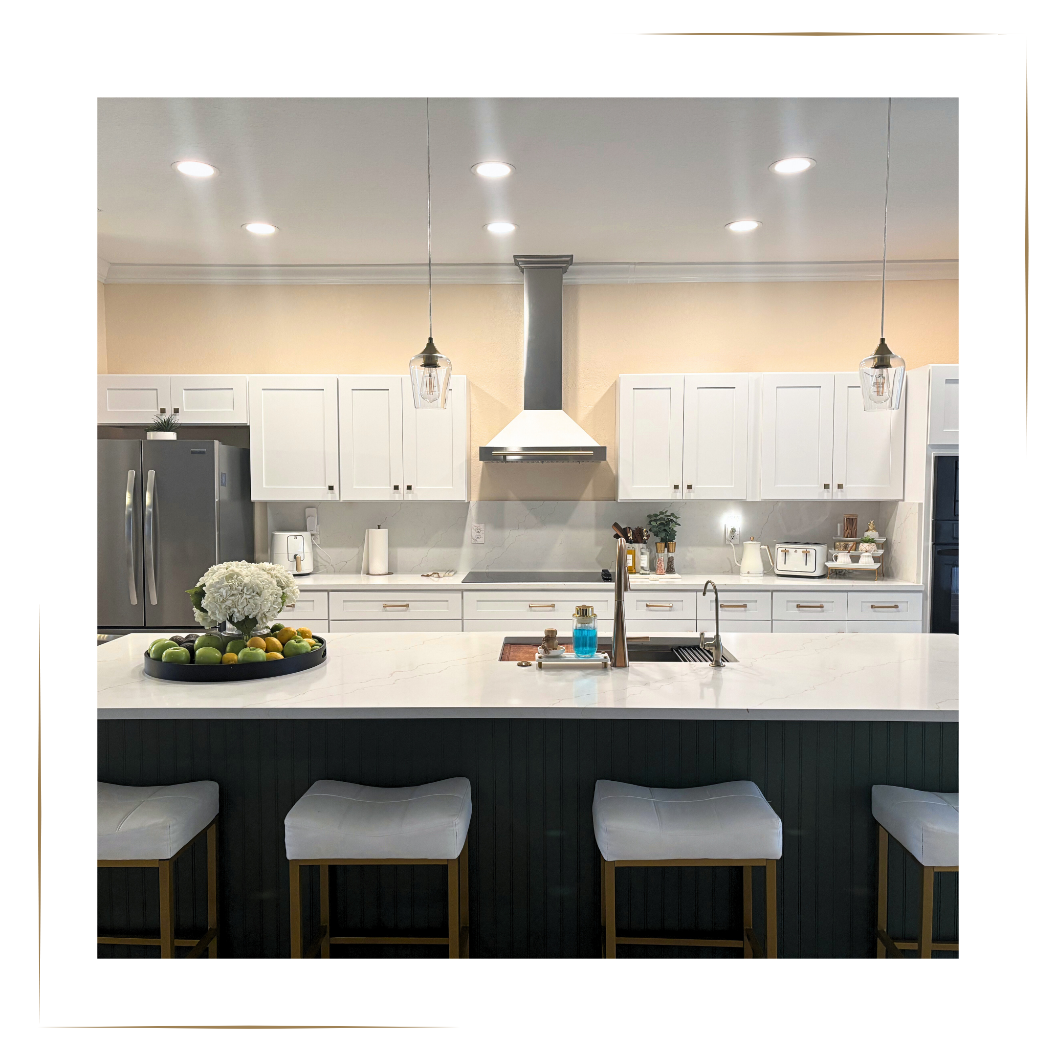 After: Modern renovated kitchen with white cabinets, a large white-marble island, stainless steel appliances, and gold-accent bar stools. Updated lighting, clean styling, and a bright, open layout showcase a high-value flip design.