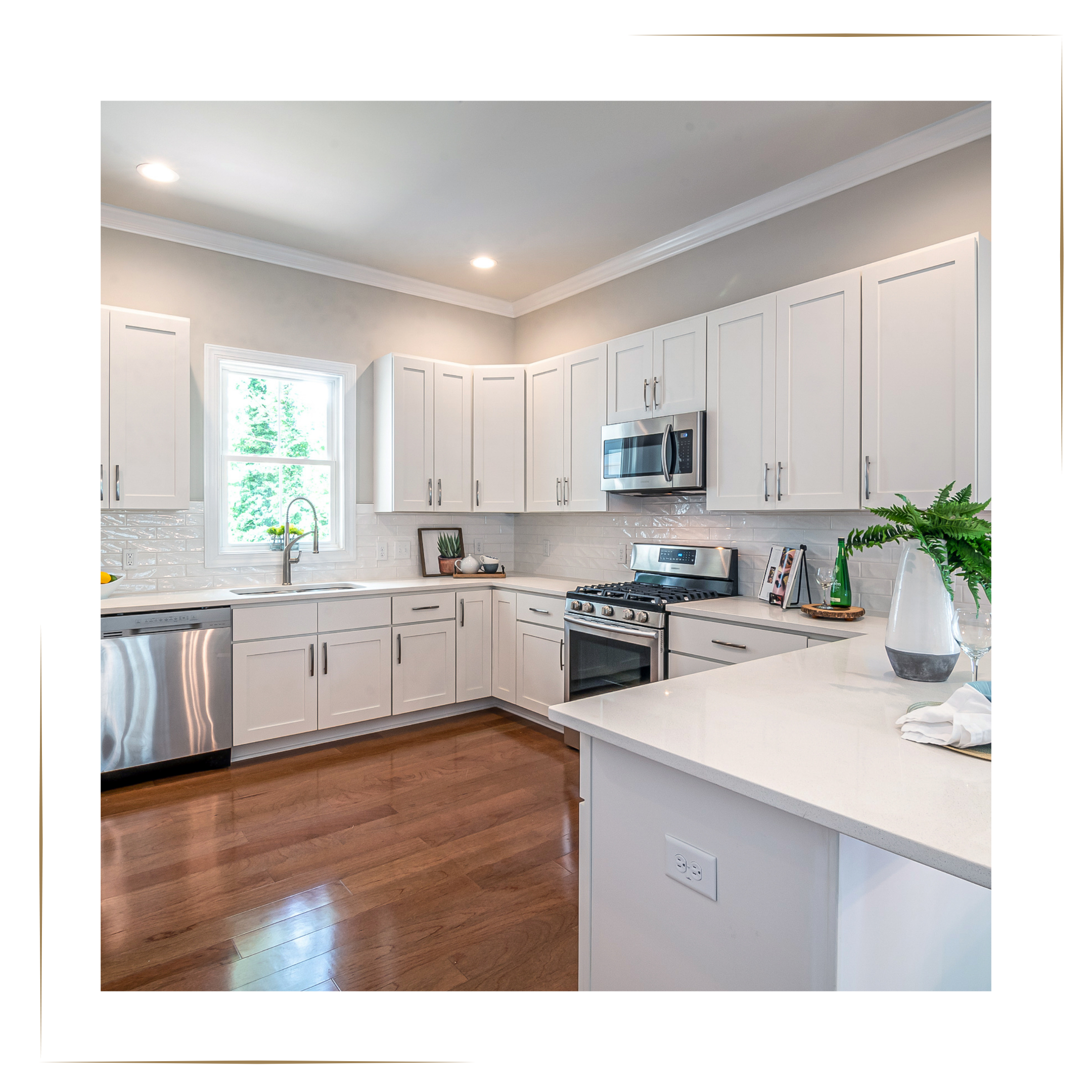 Modern kitchen with white cabinets, stainless steel appliances, hardwood floors, and a small window above the sink with greenery outside. Virtual Home Staging by Harmony Homes by Amanda