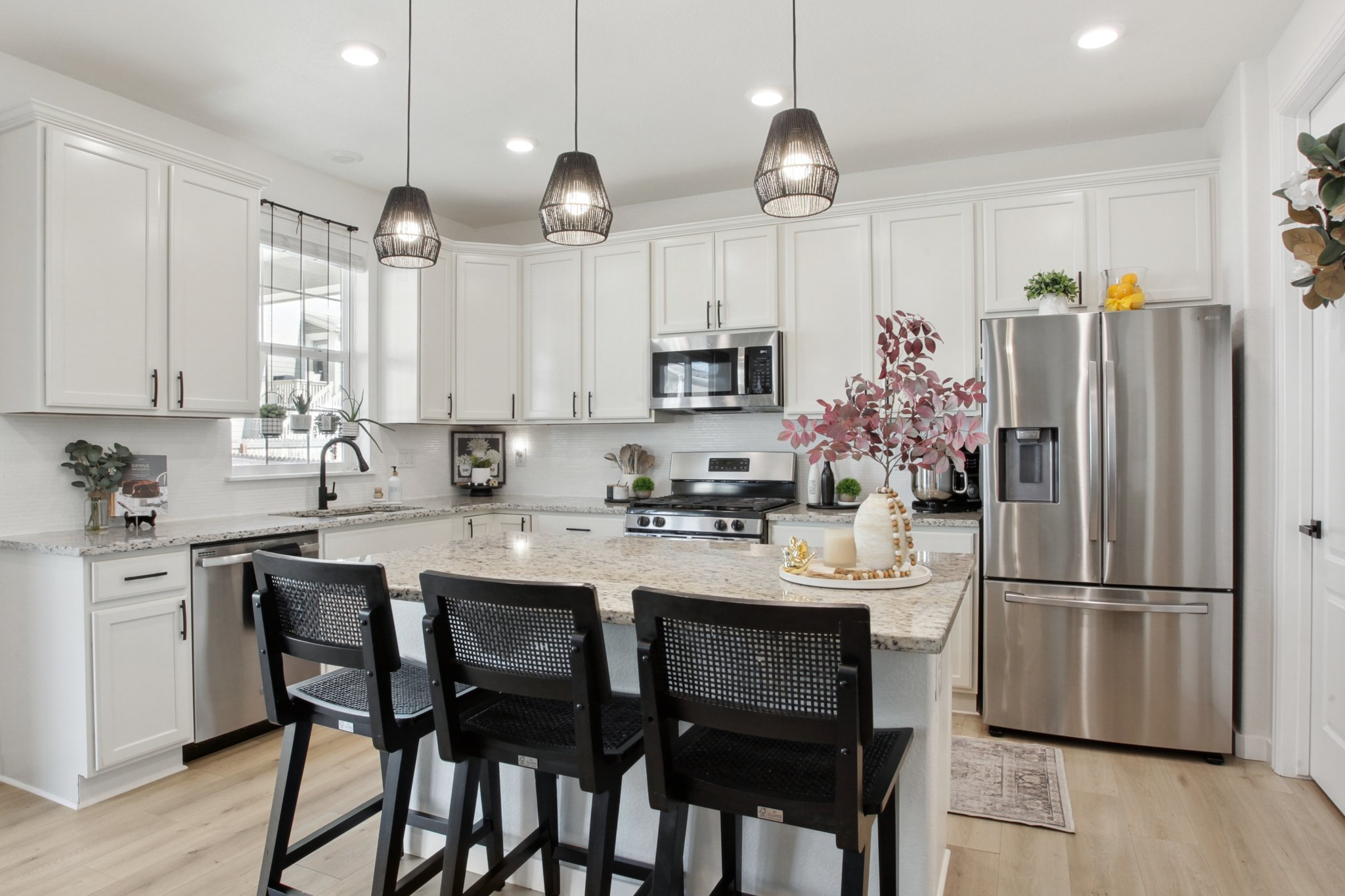 Kitchen after Flip Design and Home Staging, featuring white cabinets, stainless steel appliances, black pendant lighting, a granite island, black chairs, and simple decorative accents to improve buyer perception.