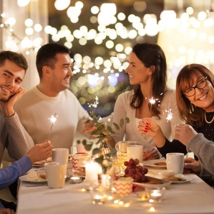 Group of friends sharing dinner and sparklers at warmly lit table.