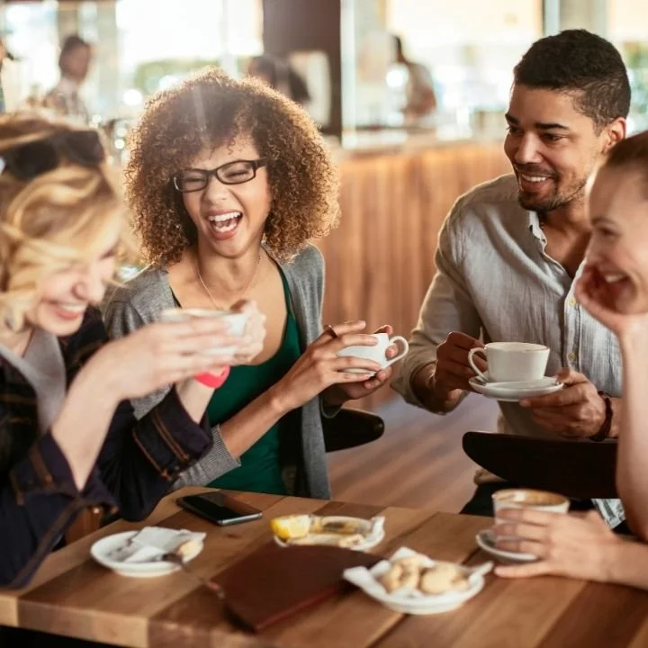 Group of friends laughing and enjoying coffee together at a table.