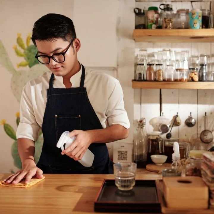 Barista cleaning a wooden counter at a coffee preparation station.