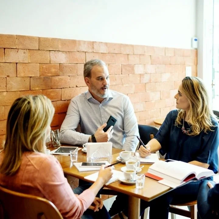 Group of adults seated at a café table wedding planning and drinking coffee.