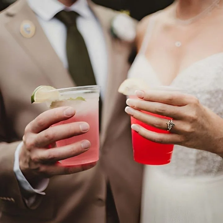 Bride and groom holding colorful non-alcoholic drinks in clear cups.