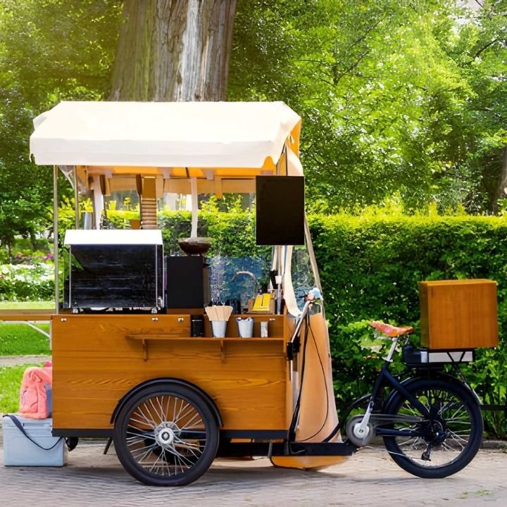 Bicycle-style coffee cart set up outdoors with wooden counter and espresso equipment.