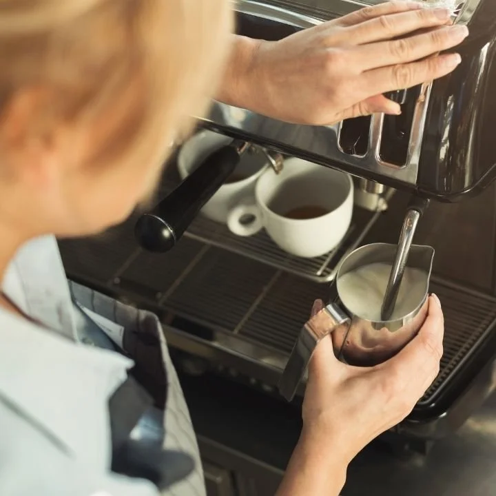 Barista steaming milk and preparing espresso at a coffee machine.