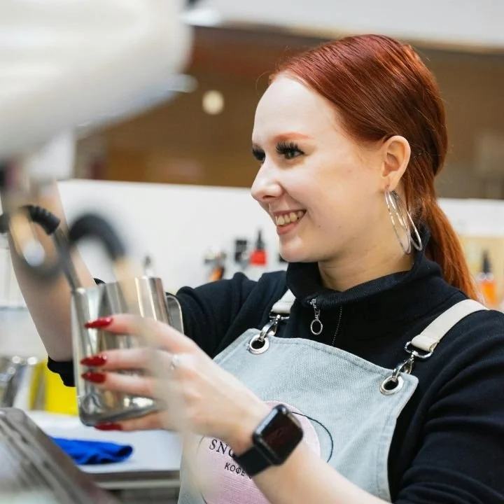 Barista smiling while steaming milk and preparing a specialty coffee drink.