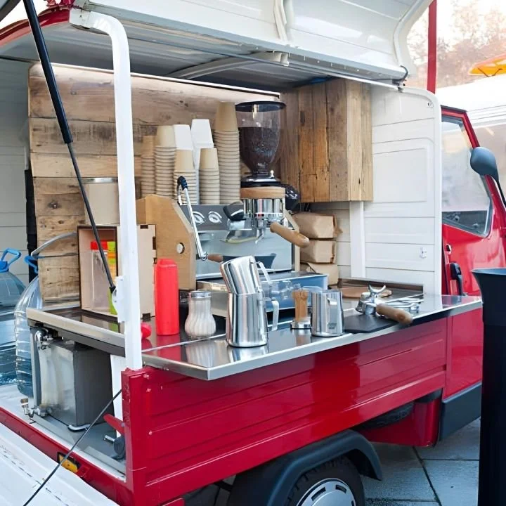 Red mobile coffee truck interior showing espresso machine, grinder, cups, and prep counter.