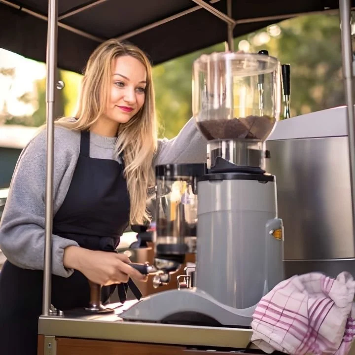 Barista operating espresso machine at outdoor mobile coffee station.