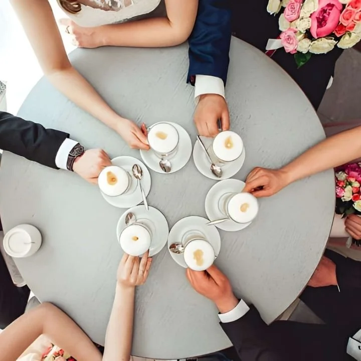 Overhead view of several hands holding coffee cups around a round table at a wedding.