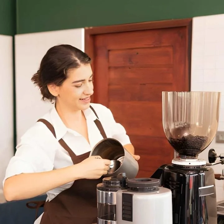 Barista measuring coffee beans into grinder before preparing espresso drinks.