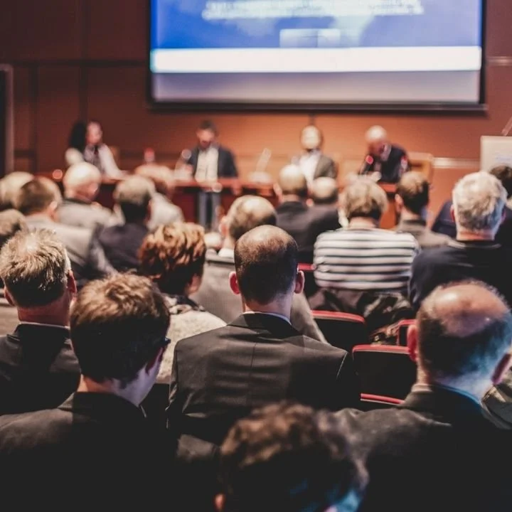 Corporate conference audience listening to speaker during large business event.