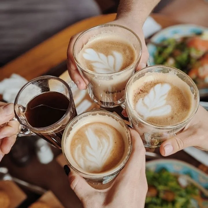 Hands raising coffee drinks together in celebratory toast at table.