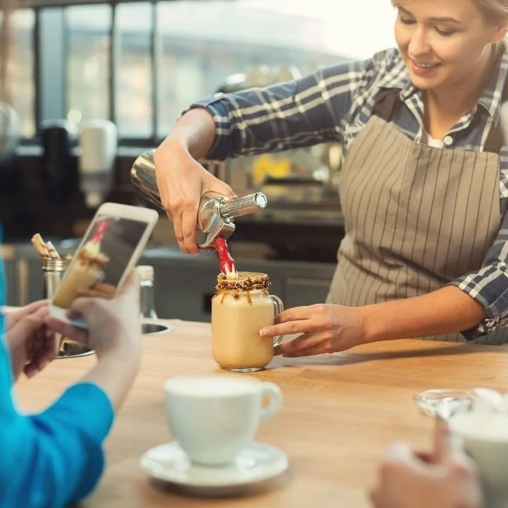 Barista pouring whipped topping onto a specialty iced coffee beverage.
