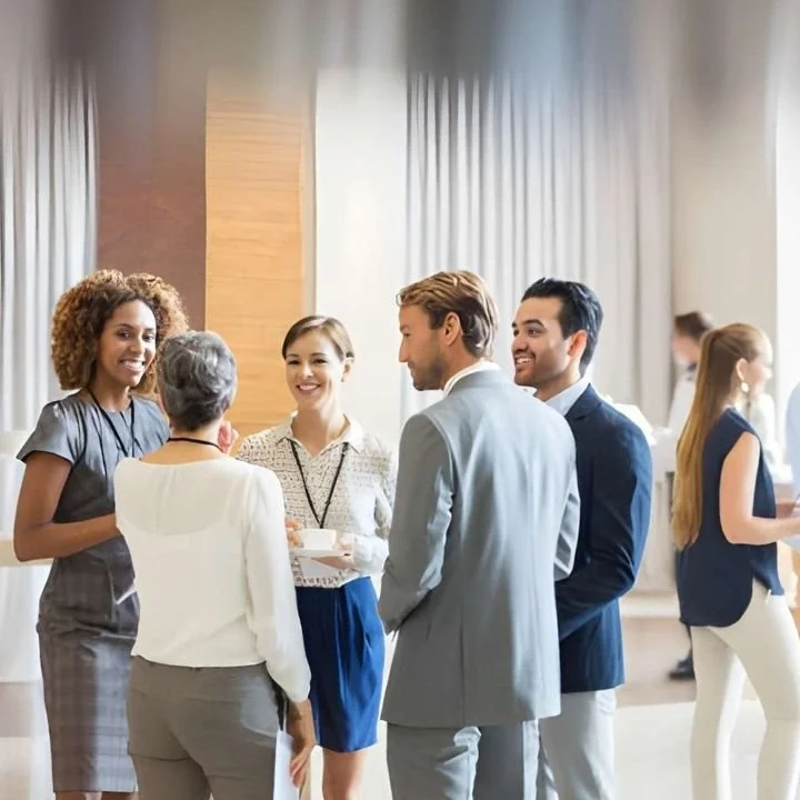 Business professionals networking at event while holding coffee cups.