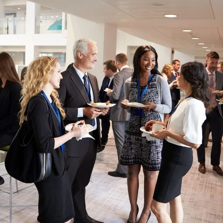Professionals networking at corporate event while enjoying catered coffee and pastries.