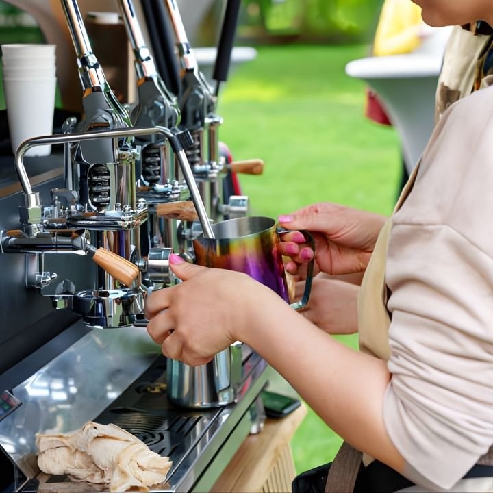 Barista steaming milk at an espresso machine set up outdoors.