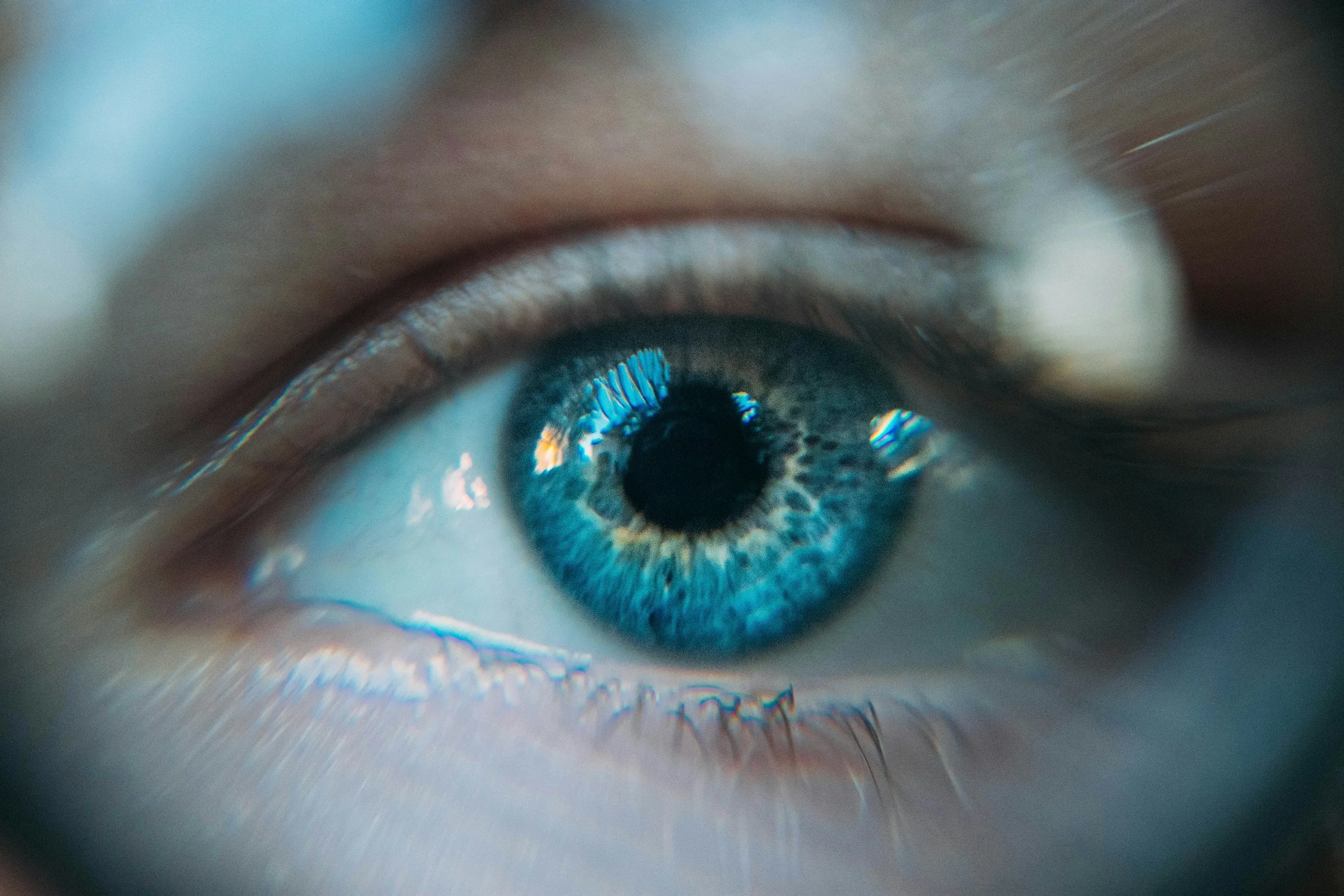 Close-up of a human eye with a blue iris, detailed eyelashes, and reflections in the cornea.